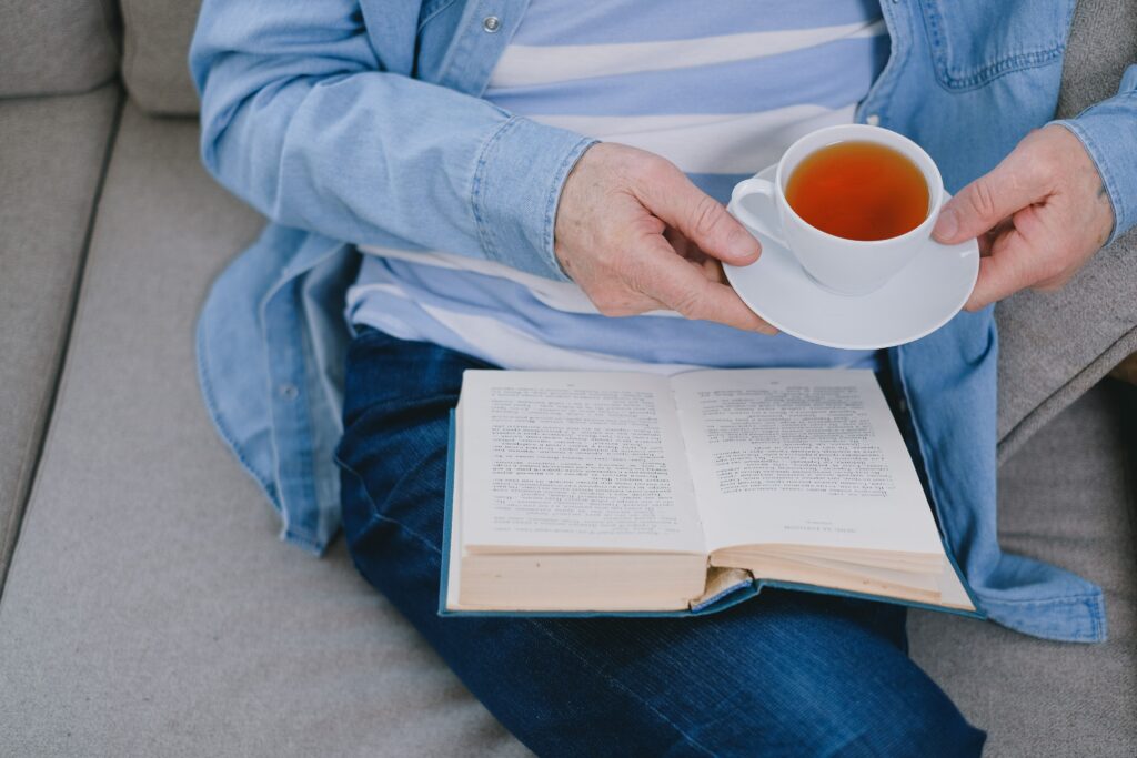 A person sitting on a couch holding a cup of tea and a book.